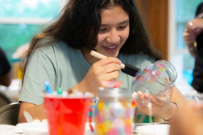 Ariel Lopez, 14, paints a thin layer of glue on a jar to decorate it with tissue paper...