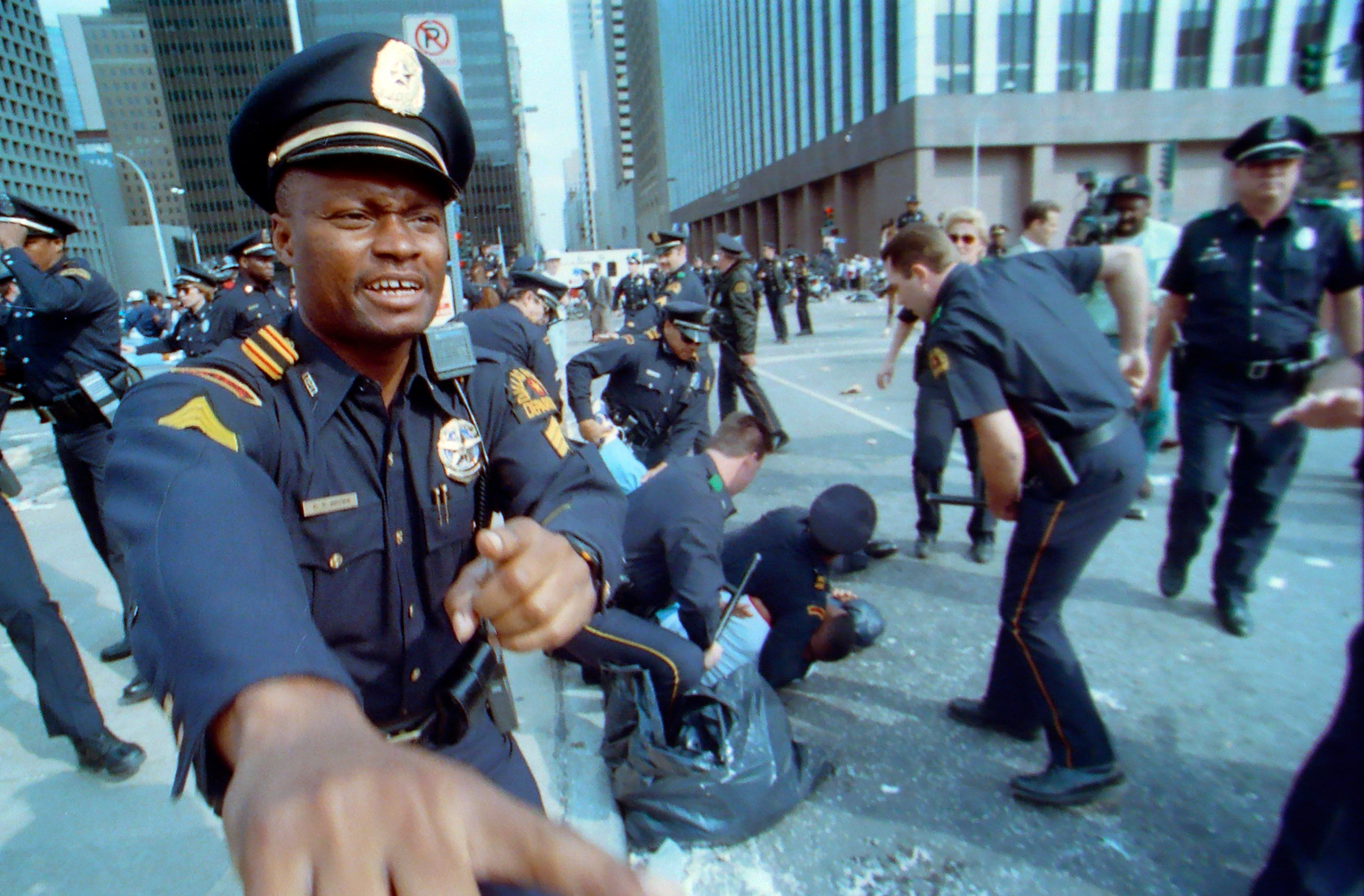 Dallas police SWAT Sgt. David Brown (left) keeps bystanders back as a man is restrained on...