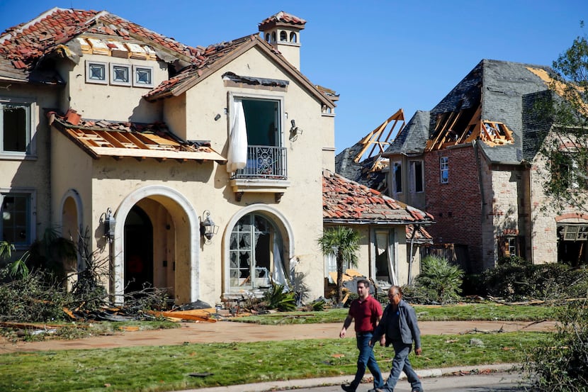 A pair of men walk by some some damaged homes on Pemberton Drive in Dallas, October 21,...