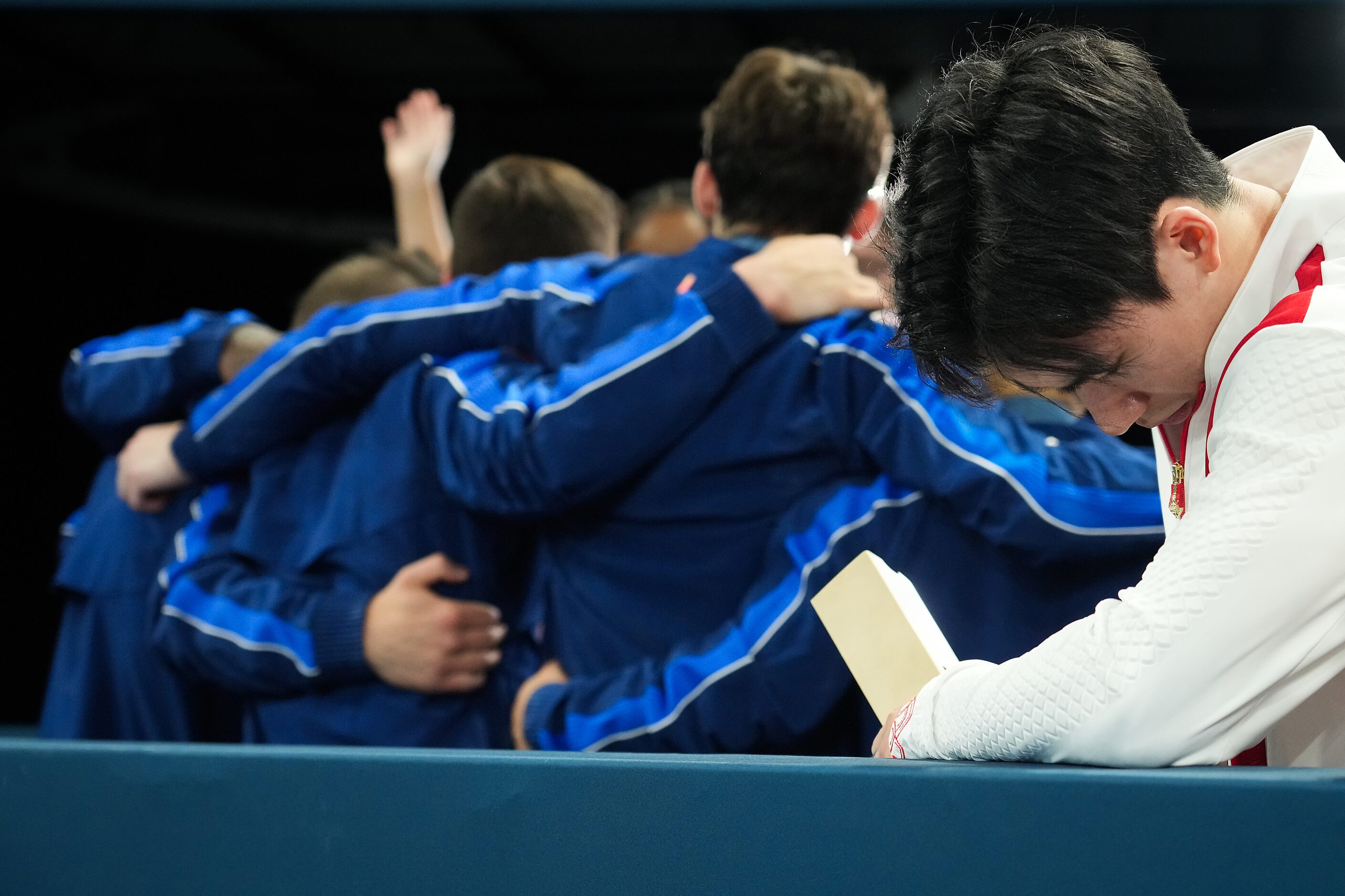 Wei Sun of China hangs his head as United States gymnasts celebrate taking the bronze medal...