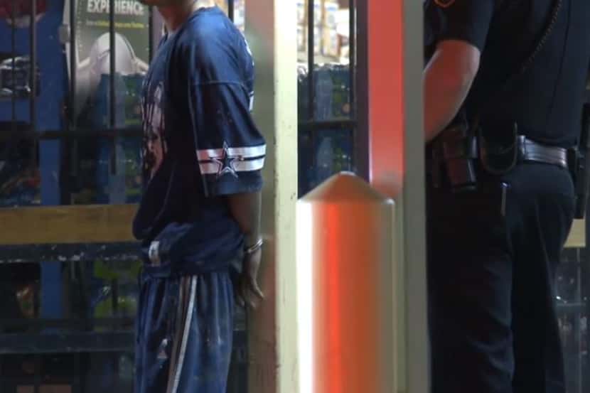 A suspect in the burglary of a grocery store waits in handcuffs as Fort Worth police search...
