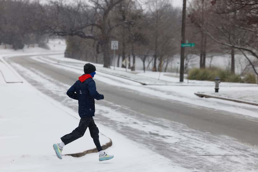 A runner crosses a snow covered Garland Road near White Rock Lake in Dallas, Monday, Jan....