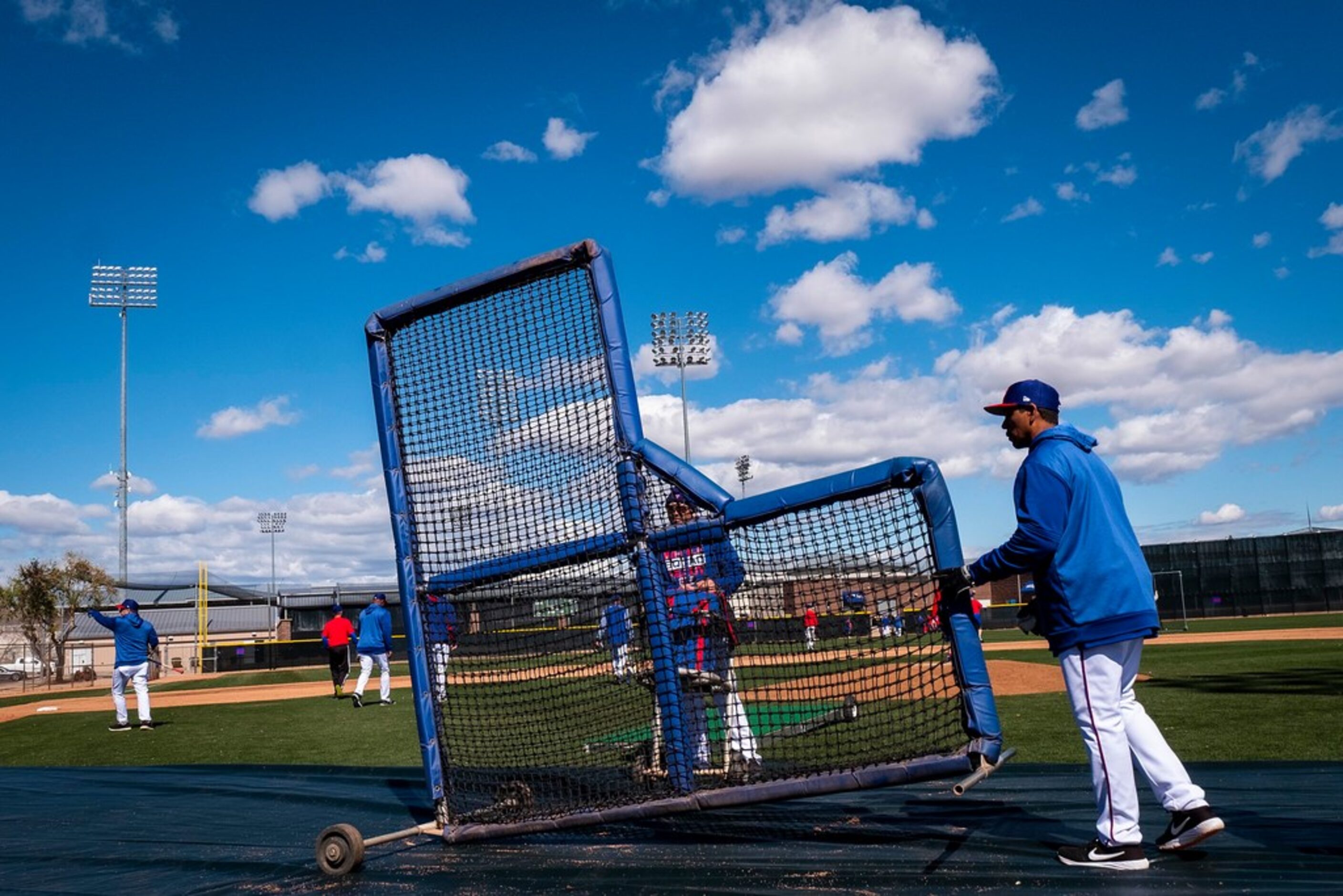 Texas Rangers hitting coach Luis Ortiz moves a batting practice screen during a spring...