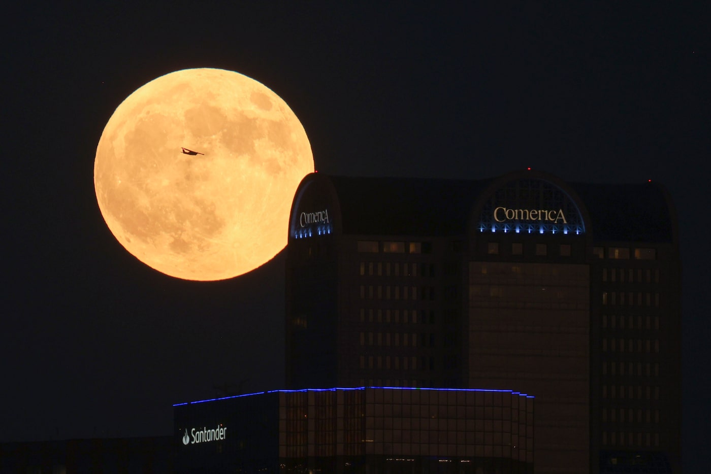 A plane passes by the full super harvest moon as it rises past Dallas’ Comerica bank tower,...