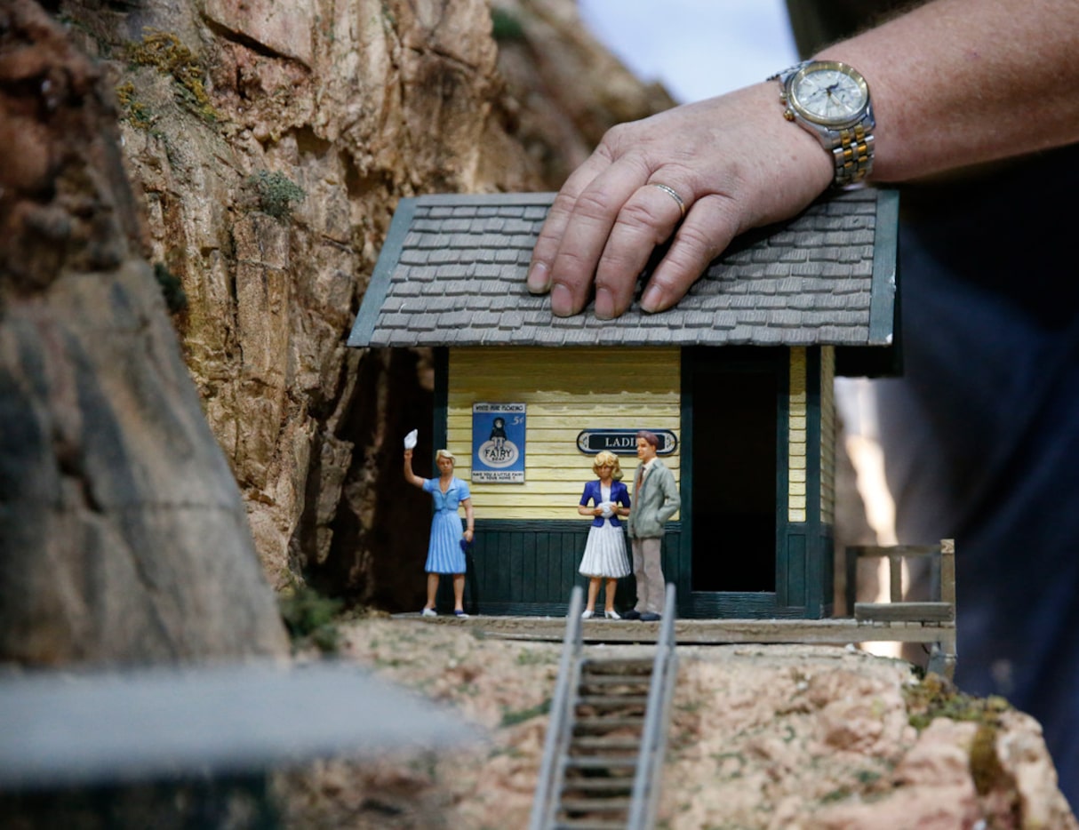 Andy Wartman uses a house as a brace as he paints texture on the mountains in the Museum of...