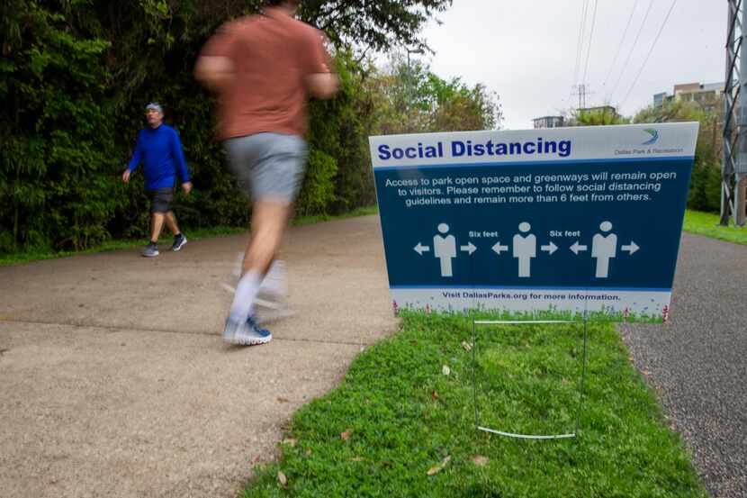Joggers on the Katy Trail in Dallas ran past a sign advising social distancing measures on...