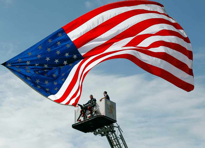 An American flag flies from extended fire truck ladders for Thursday's procession from West...