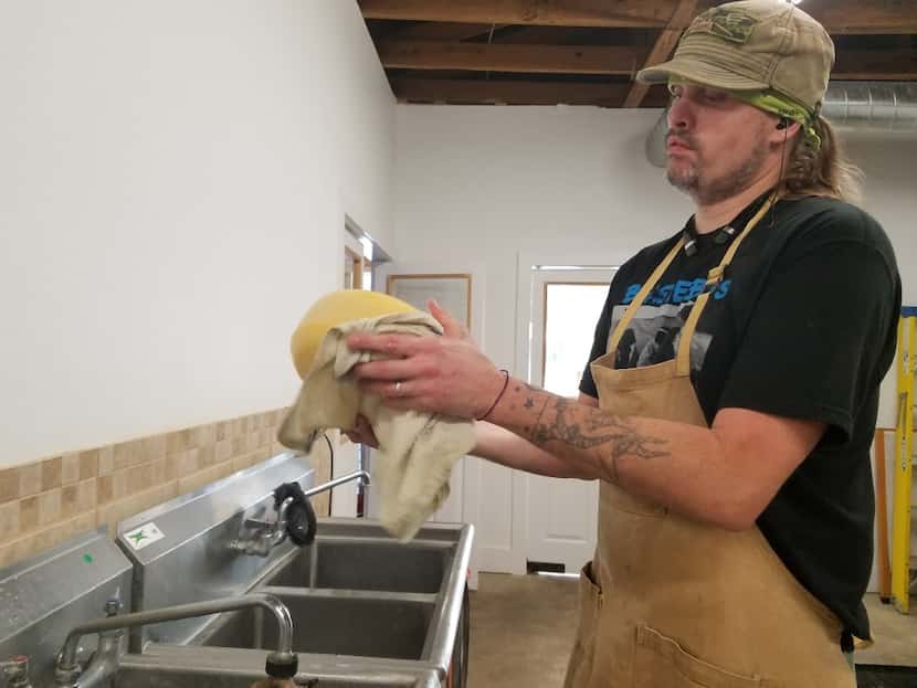 Matt Eagle washes a cheese at Eagle Mountain Farmhouse Cheese in Lipan. During its aging,...