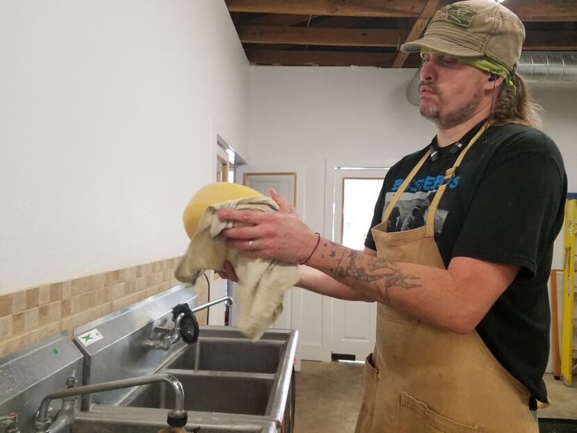 Matt Eagle washes a cheese at Eagle Mountain Farmhouse Cheese in Lipan. During its aging,...