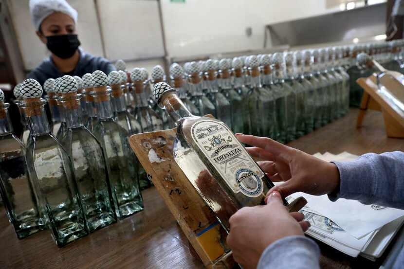 Trabajadores colocan etiquetas a mano en botellas de tequila en la destilería de tequila...