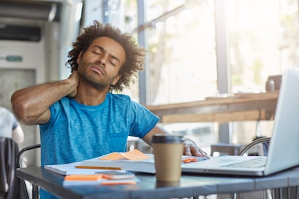 Young tired manager sitting in restaurant surrounded with papers and laptop computer having...