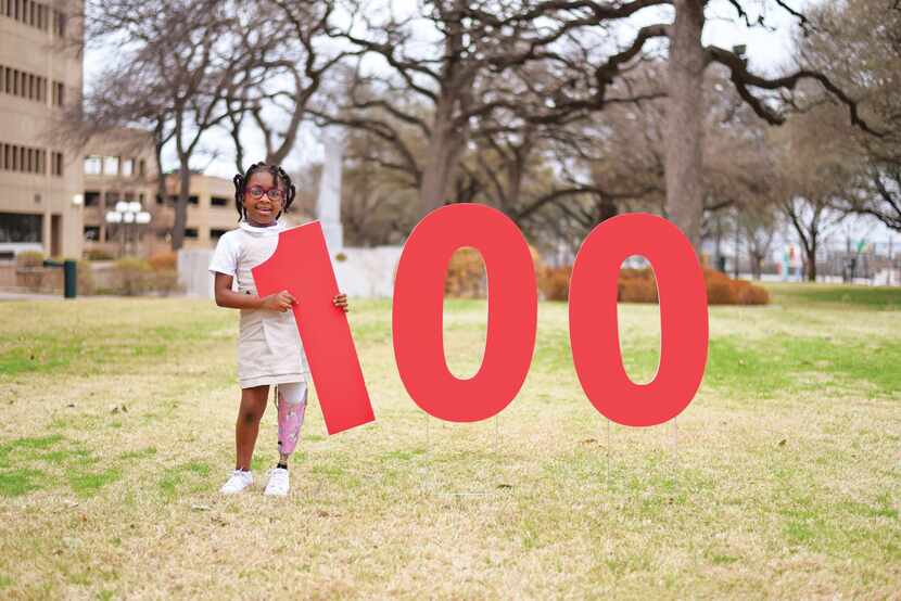 A child wearing a prosthetic poses with a sign that spells out 100 in honor of Scottish...