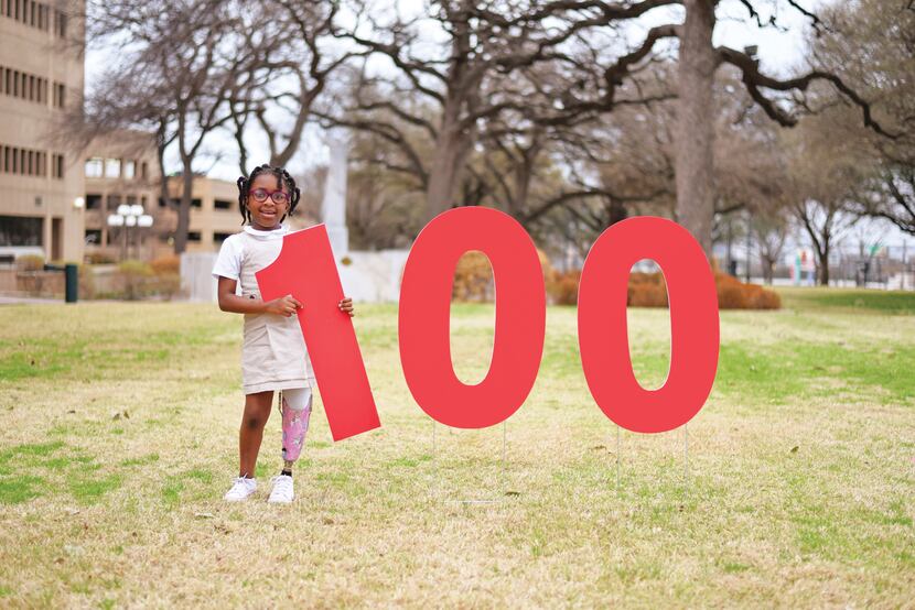 A child wearing a prosthetic poses with a sign that spells out 100 in honor of Scottish...