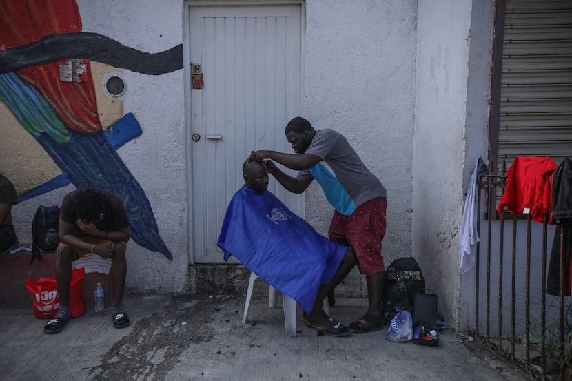 Un hombre corta el cabello a otra persona en un centro de refugio para migrantes en...