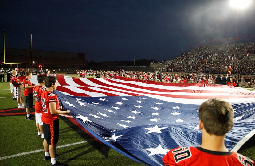 The Coppell High School freshman football team drapes a flag across the field for the...