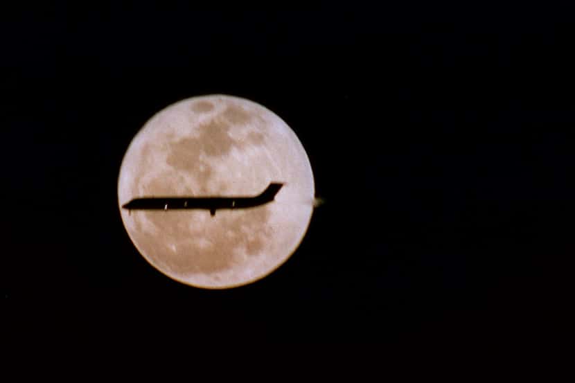 A full moon illuminates a plane's landing at DFW Airport.