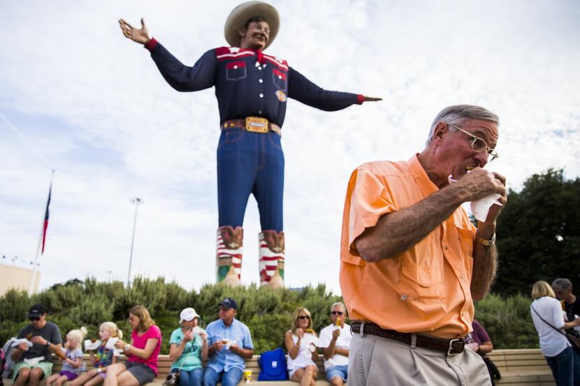 A man eats a Fletcher's Corny Dog as he passes Big Tex on October 7, 2015 at the State Fair...
