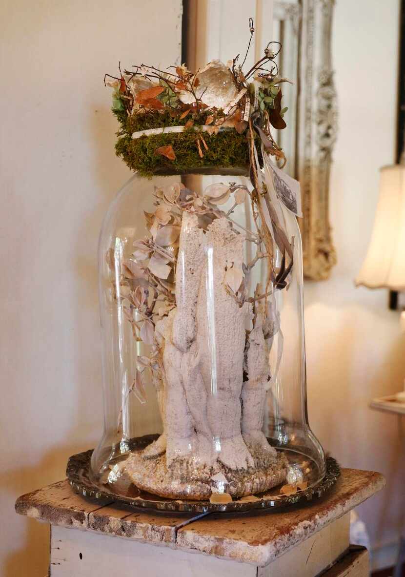 
A distressed statue under a cloche is topped with a crown made of leaves and moss. Putting...
