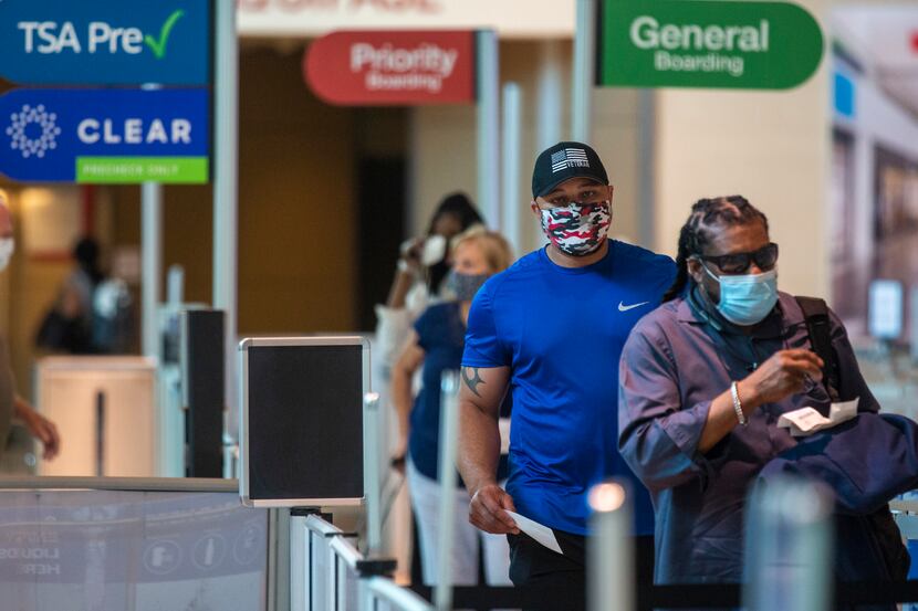 Masked passengers walk to the security checkpoint at Dallas Love Field airport in Dallas on...