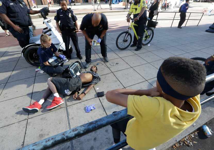 A man lies handcuffed and unresponsive as first responders attend to him at a DART rail stop...