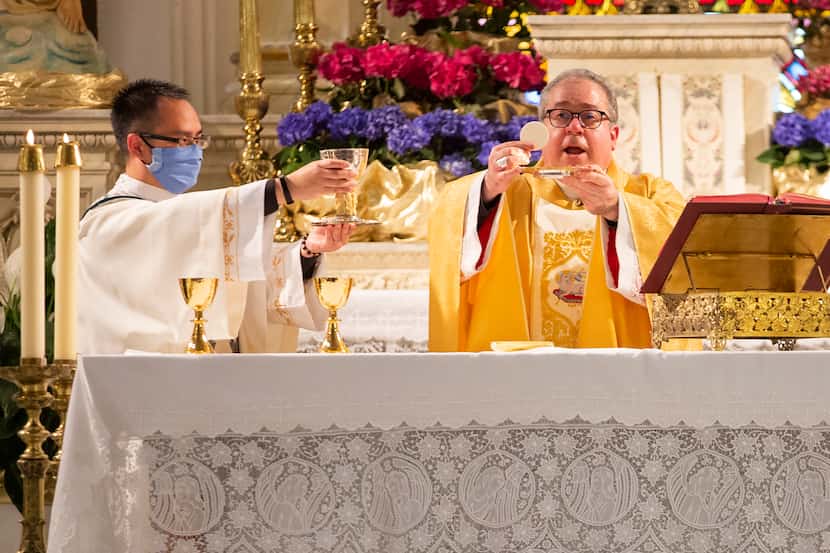 Bishop Michael Olson (right) and deacon Linh Nguyen consecrate the host during mass at St....