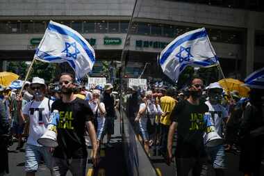 Demonstrators march with Israeli flags during a protest marking nine months since the start...