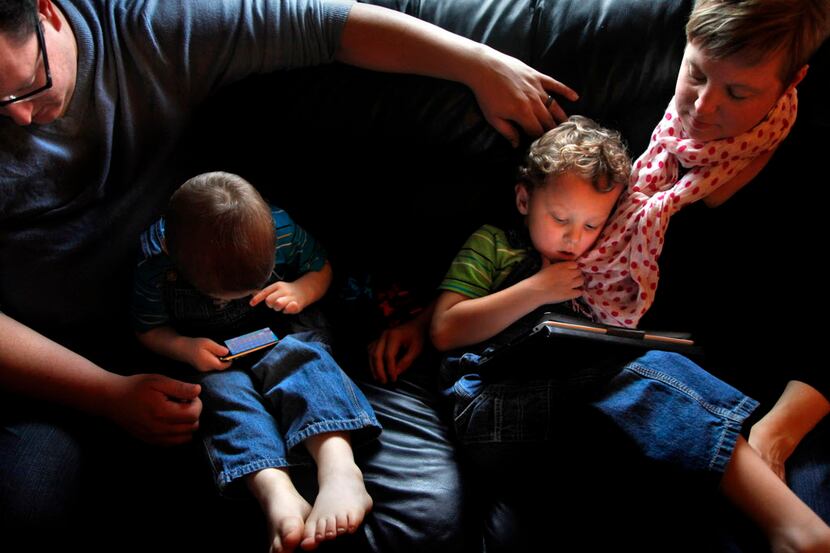 Parents relax with 3- and 4-year-old sons as the kids play with an iPhone and an iPad at...