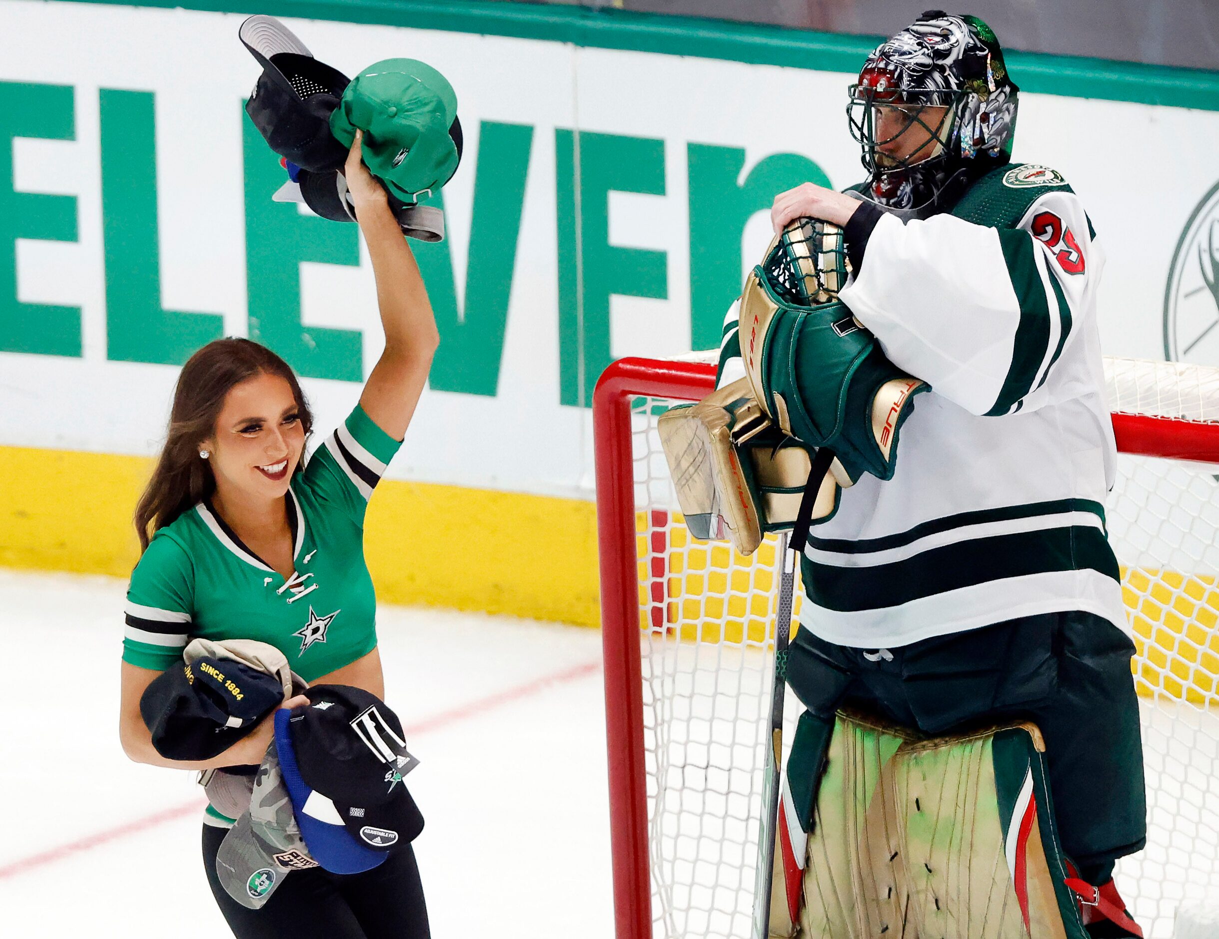 A Dallas Stars Ice Girl collects hats off the ice in fort of Minnesota Wild goaltender...