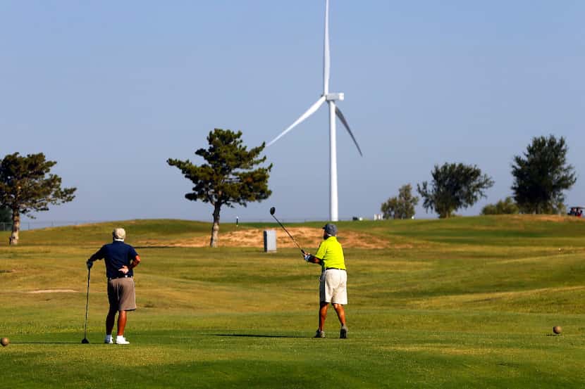 Golfers tee off before a large wind turbine at the Reese Golf Center in Lubbock, Texas,...