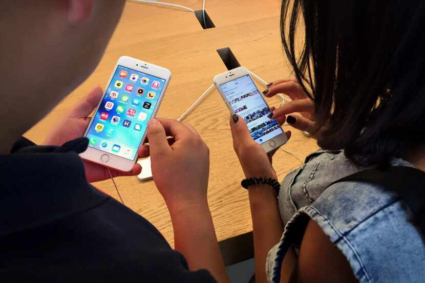 Customers try out Apple iPhone 6S models on display at an Apple Store in Beijing, Saturday,...
