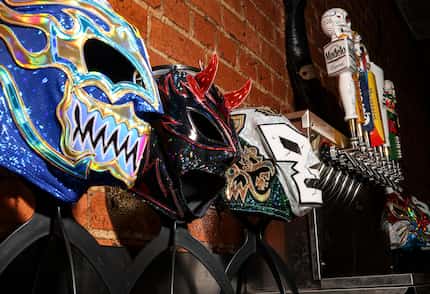 Masks line the wall near the bar at El Taco H. The bar menu includes Mexican beers, mezcal...