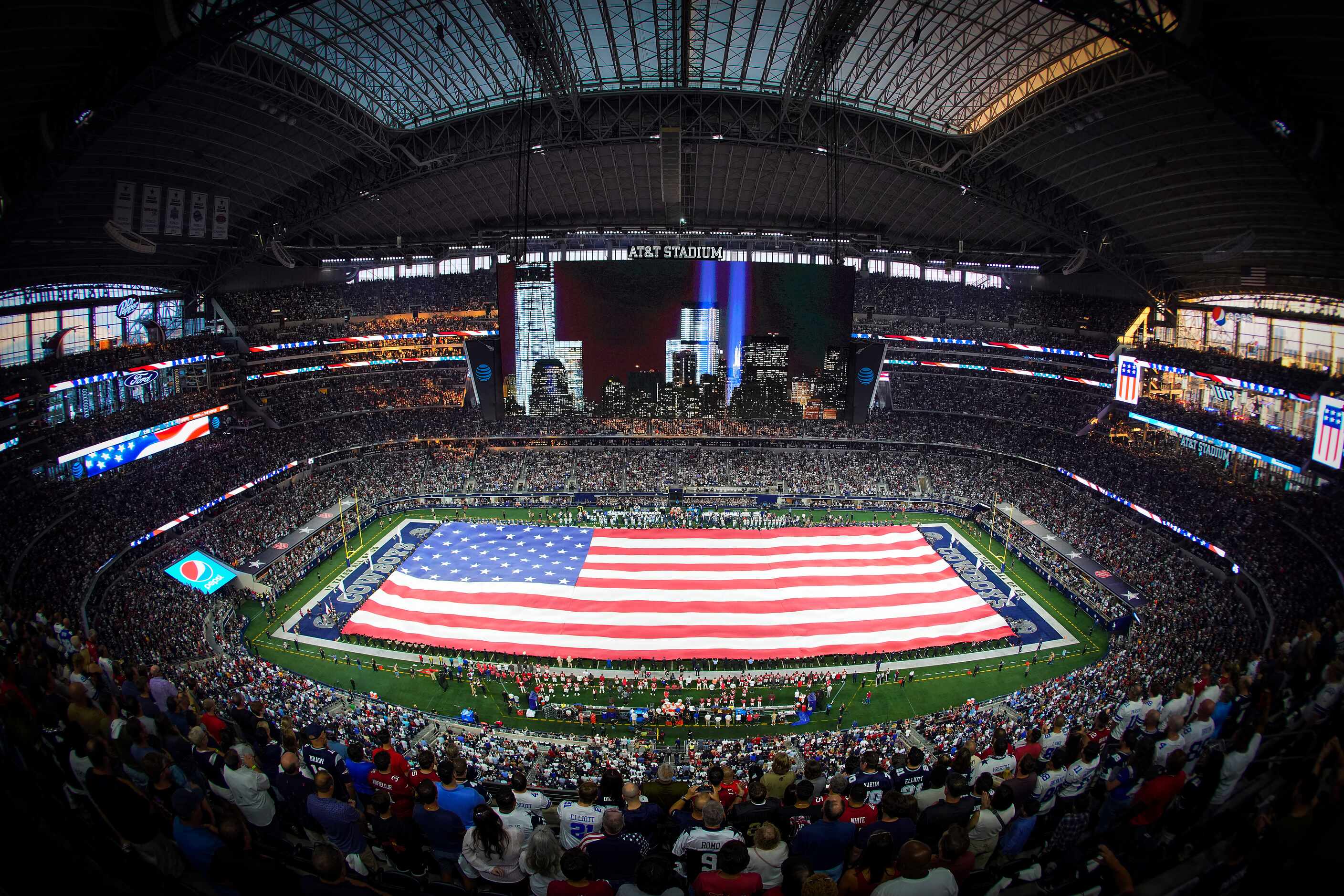 A large American flag covers the field during national anthem before an NFL football game...