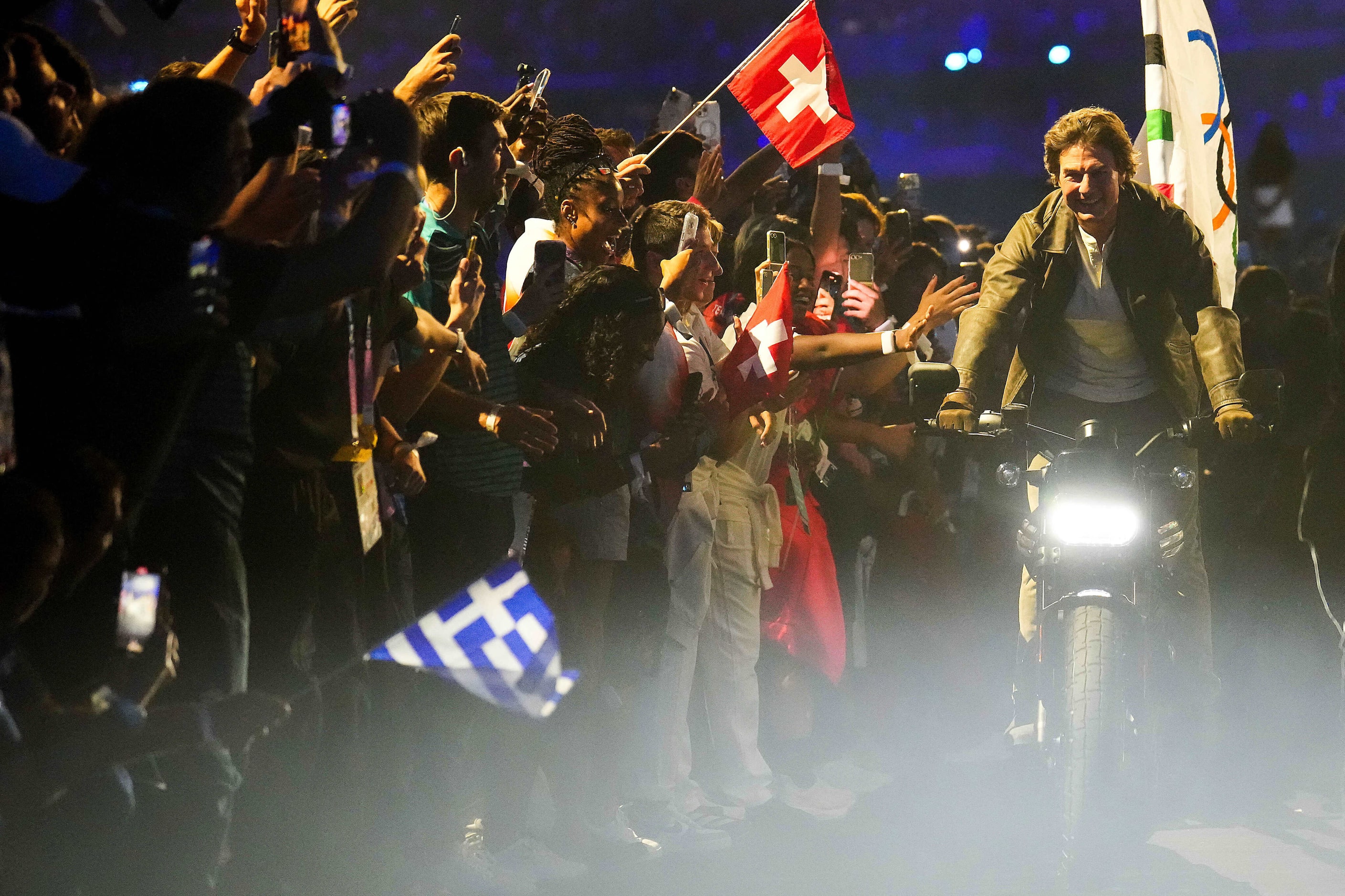 Actor Tom Cruise rides through athletes on a motorcycle carrying the Olympic flag after a...