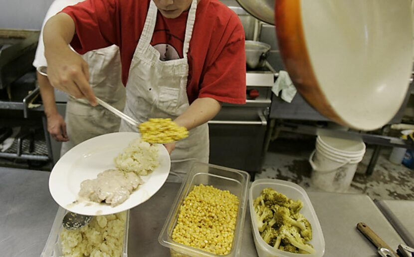 A kitchen worker in the 24 Hour Club's restaurant fills a plate. The kitchen serves...