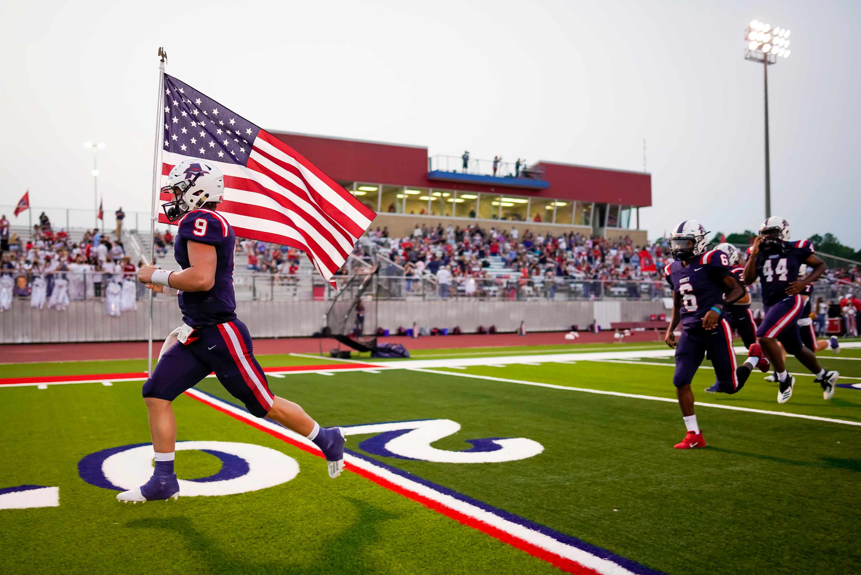 Aubrey quarterback Jaxon Holder carries the American flag as he leads his teammates onto the...
