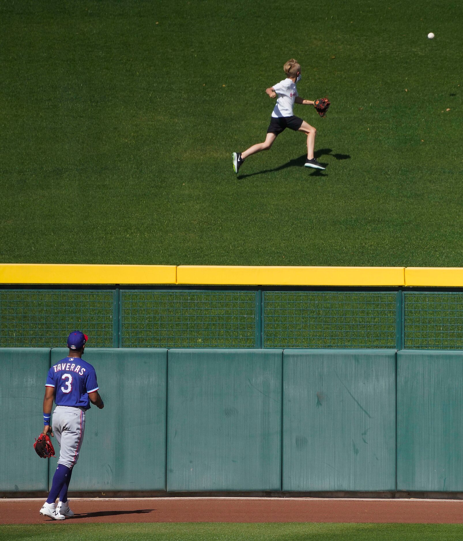 Texas Rangers center fielder Leody Taveras watches as young fan chases the ball on a grand...