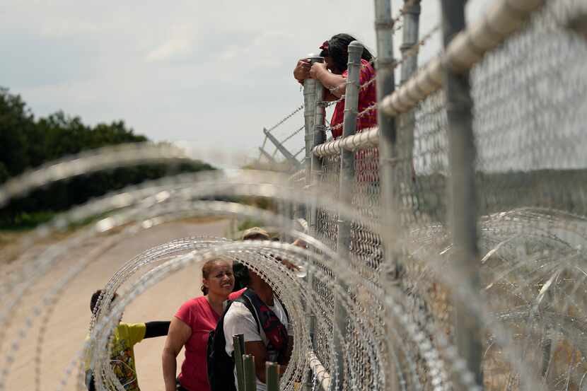 Migrants who crossed the Rio Grande from Mexico into the U.S. climbed a fence with barbed...