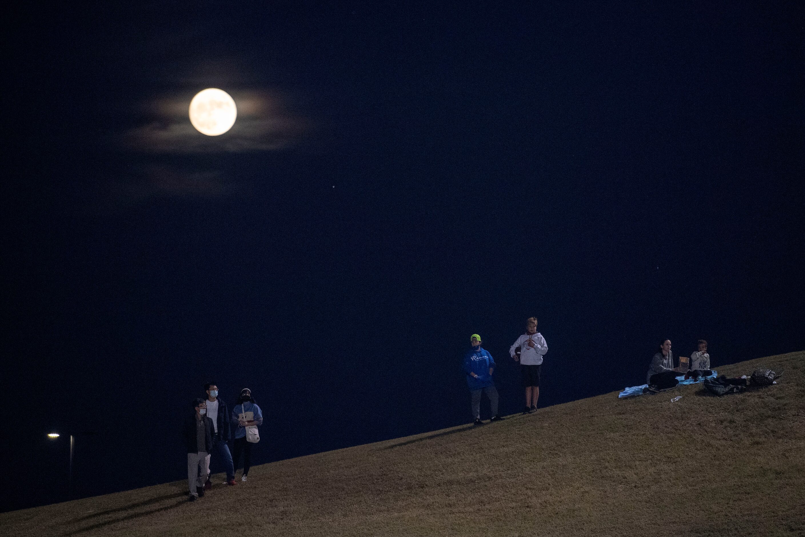 Fans watch from a hillside outside Buddy Echols Stadium as the moon rises during the first...