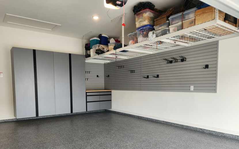 Garage with ceiling racks holding bins and boxes, and slat wall and cabinets.