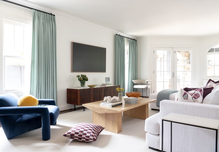 Living room with smooth white walls, blue-green curtains, a TV on the wall and a blue chair...