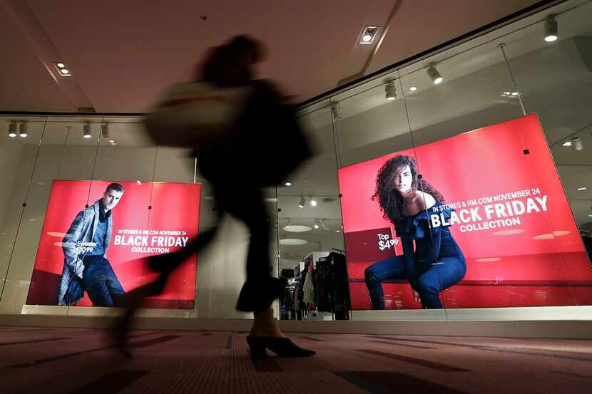 A woman with shopping bags walks by Black Friday sale signs at an H&M store at Galleria Dallas.