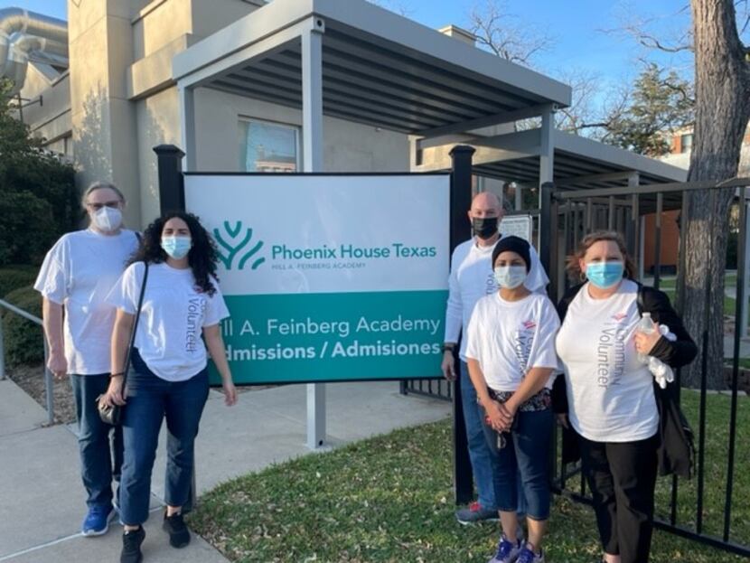 Volunteers wearing face masks stand around a Phoenix House Texas sign outside a white building.