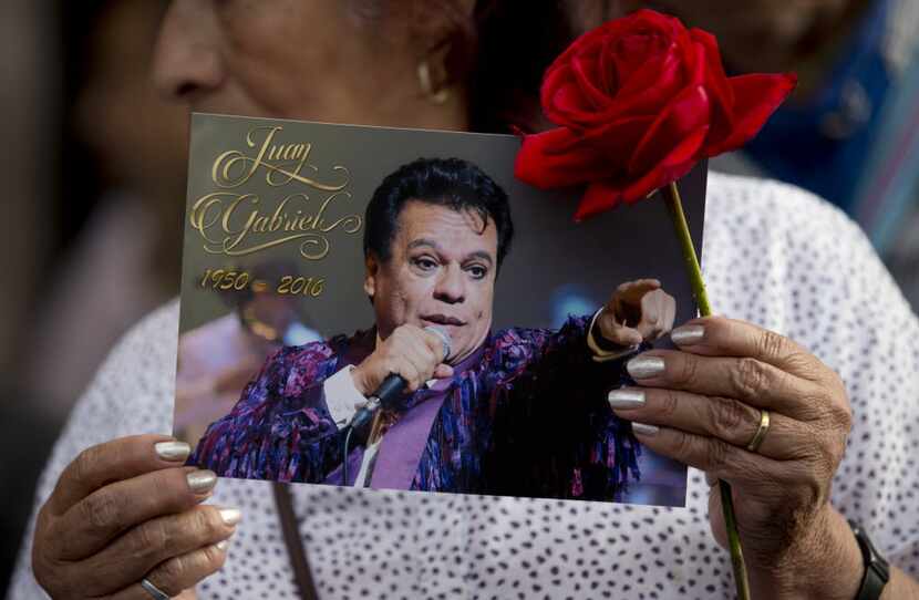A woman holds a picture of Mexican songwriter and singer Juan Gabriel near a statue of him...