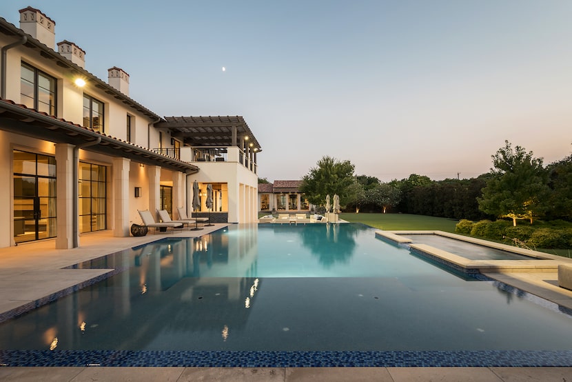 A large pool reflects the lights coming off of the home in the backyard of this house on...