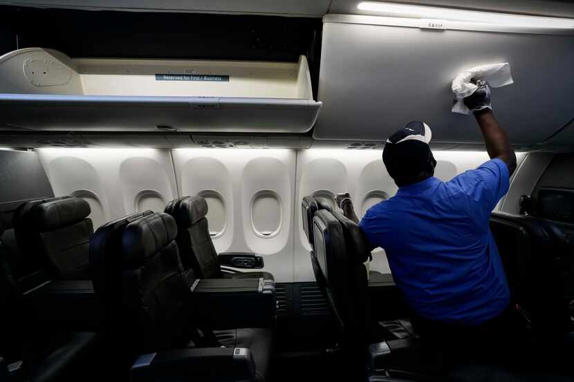 A cabin cleaner with ABM Aviation wipes down the overhead bins of an American Airlines...