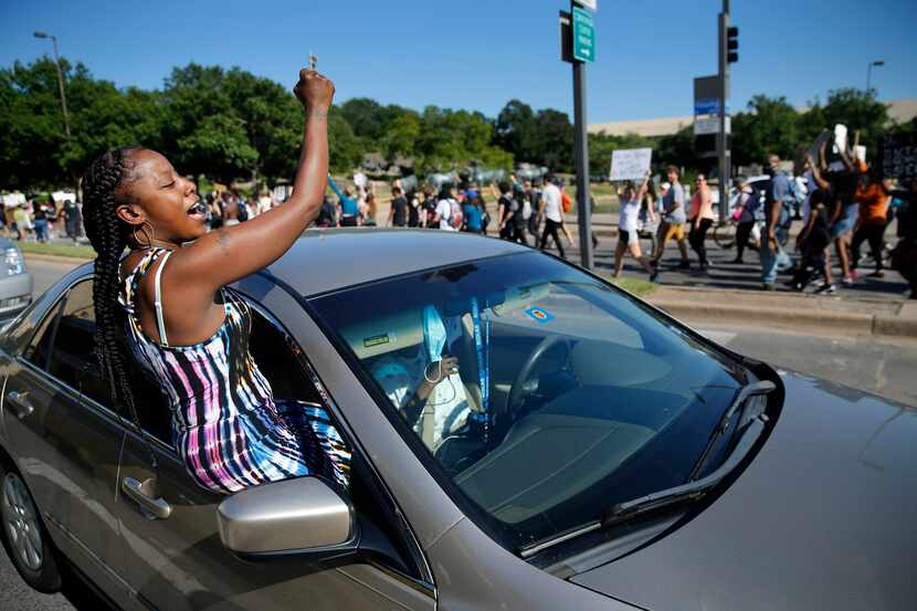 Angel Brown of Dallas crawls out of her car window to support protesters marching in Dallas...