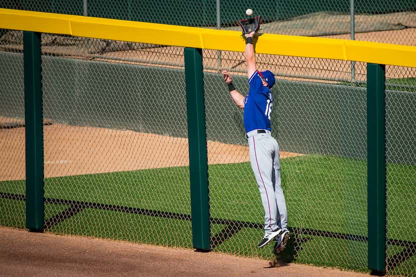 Texas Rangers right fielder Ryan Rua reaches over the wall to take a home run away from...