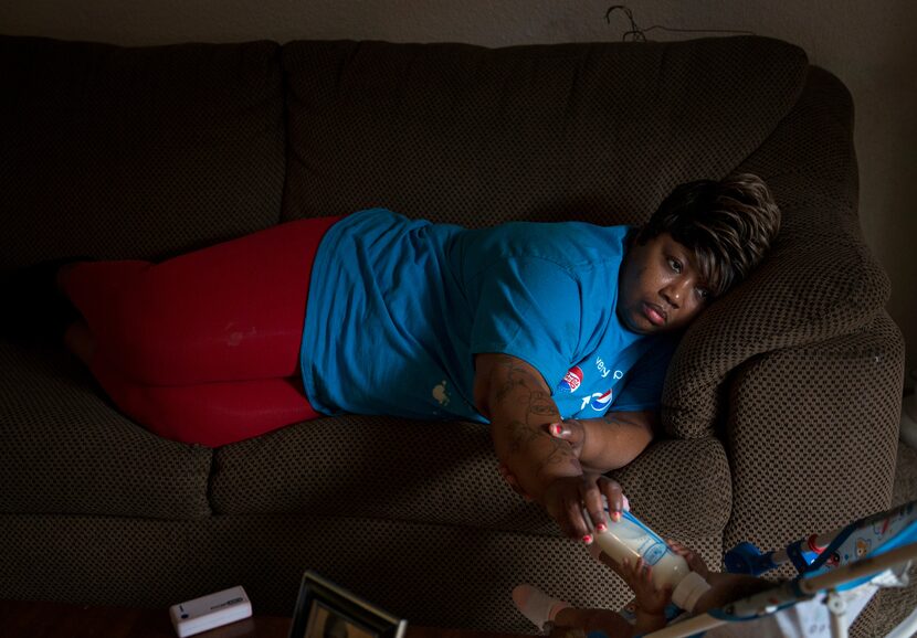 After a long day of work, an exhausted Janice Hensley lays on the couch while feeding her...