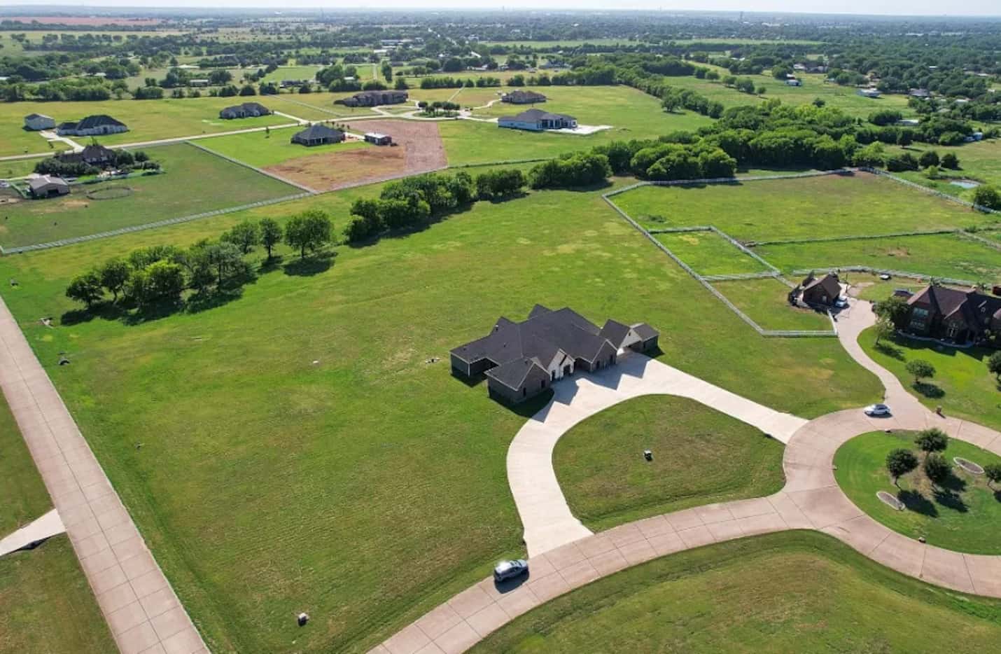 Overhead view of large home on multi-acre lot with green grass and a row of trees