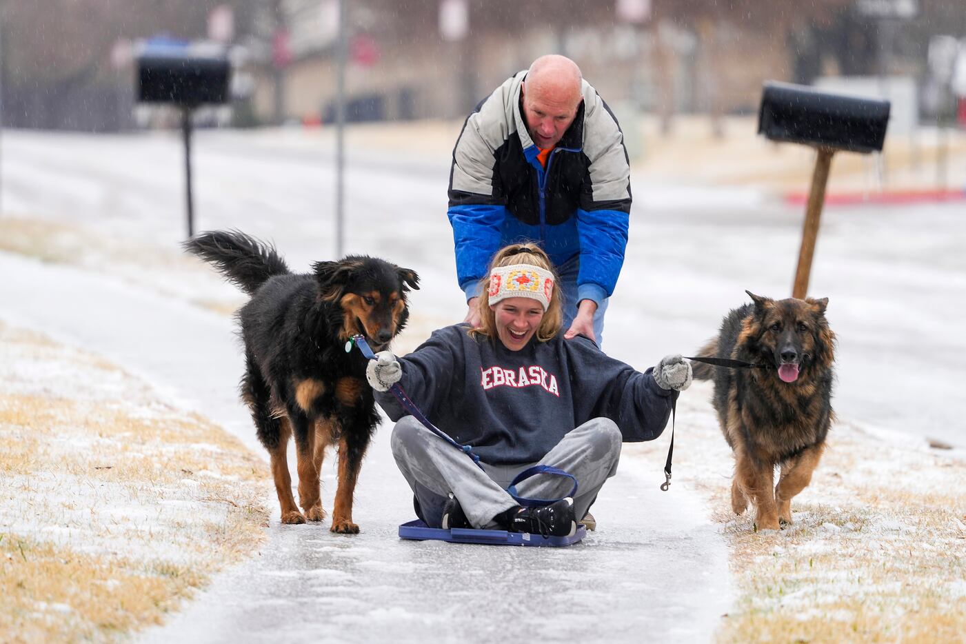 Kelsey Vining gets a push from Court Vining as she sleds down an icy sidewalk with dogs Mr...